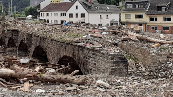 Blick auf das Flussbett und eine völlig zerstörte Eisenbahnbrücke in Band Neuenahrt-Ahrweiler nach der Flutkatastrophe im Juli 2021 - im Hintergrund zerstörte Häuser.