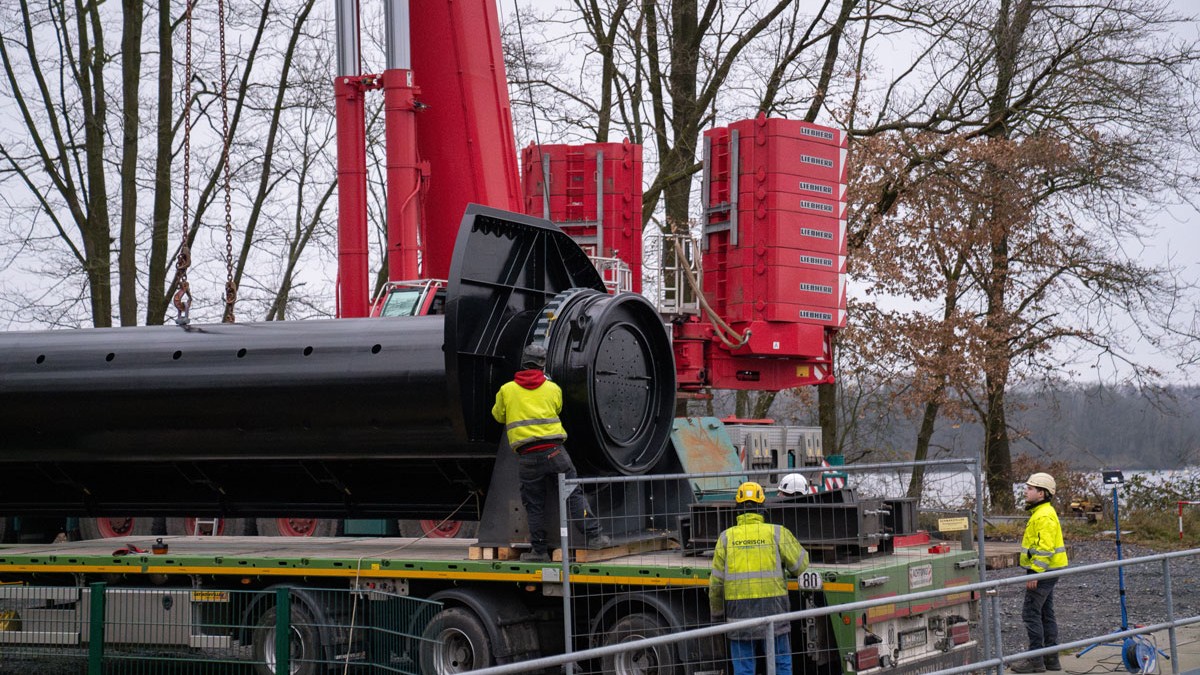 Hier wird die erste der beiden neuen Stahlwalzen per Schwertransporter angeliefert. Um die Walze vom Transporter auf das Wehr zu haben, war ein 450-Tonnen-Kran notwendig.