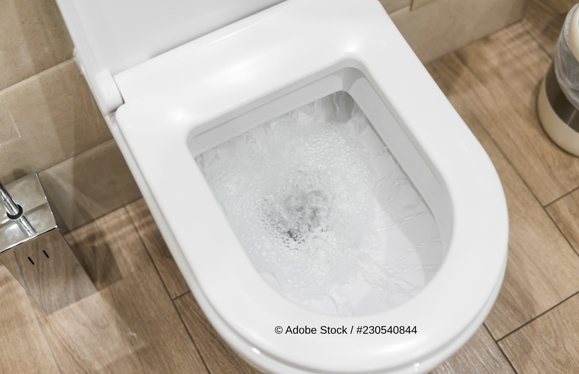 Blick in eine weiße Toilettenschüssel, in der sich das Wasser dreht.