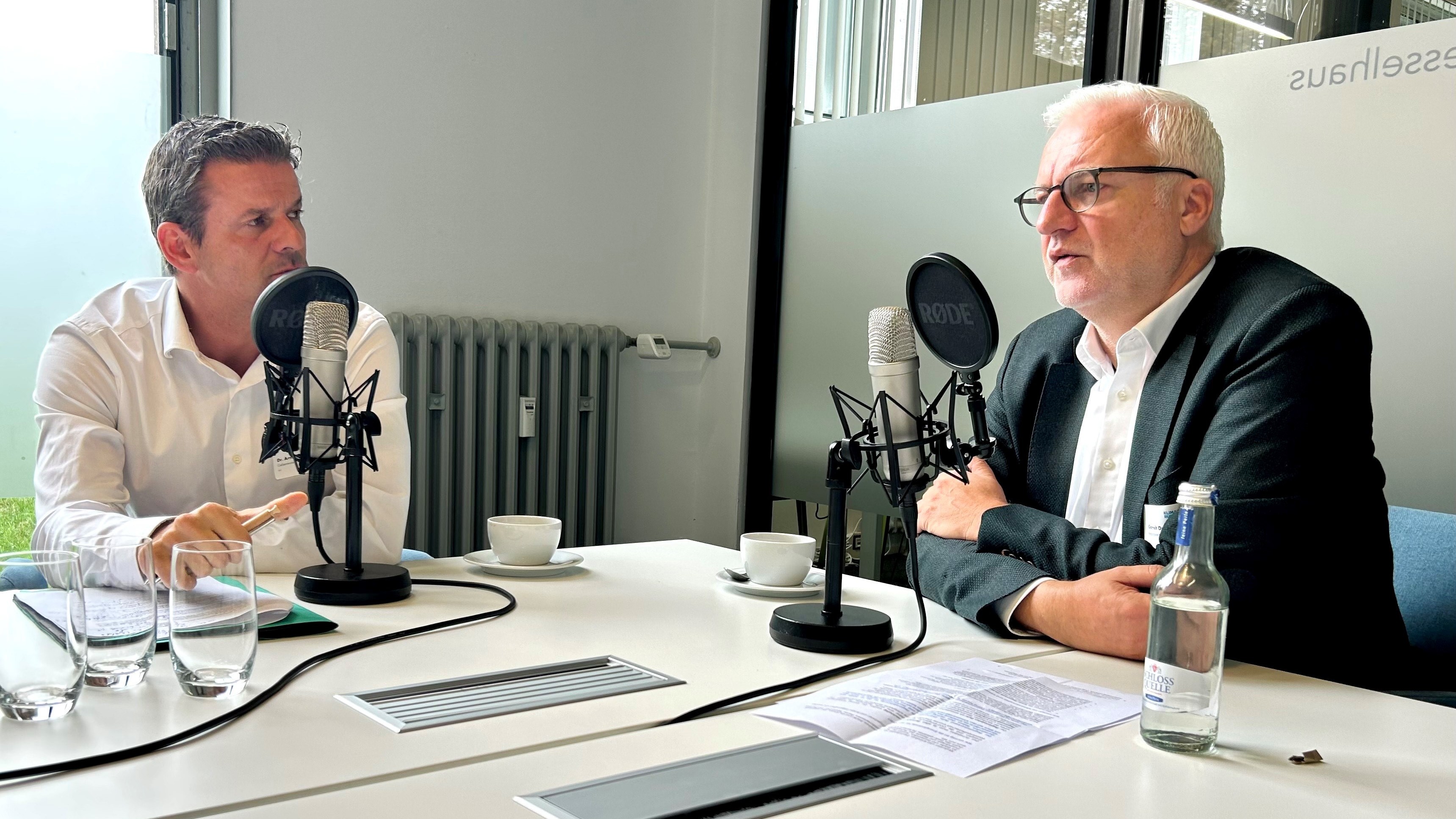 Dr. Arnt Baer von Gelsenwasser und Garrelt Duin vom Regionalverband Ruhr sitzen in einem Raum und nehmen die Podcast-Folge auf - vor ihnen stehen Mikrophone auf einem Tisch.