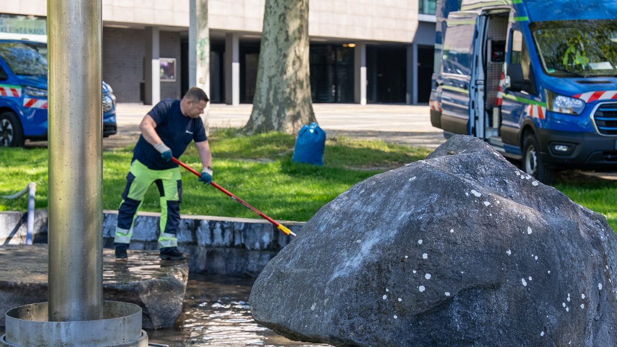 Ein Gelsenwasser-Mitarbeiter steht im Zierbrunnen vor dem MiR und reinigt den Boden.