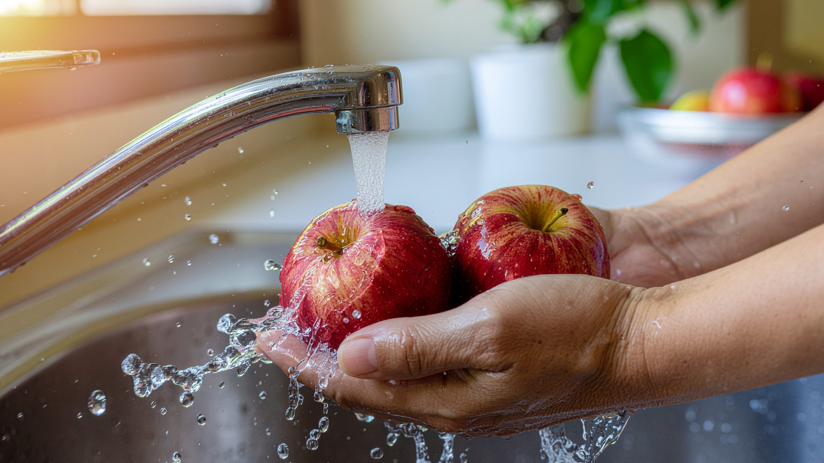 Eine Hand wäscht zwei Äpfel unter dem Wasserhahn in einer Küche mit Leitungswasser.