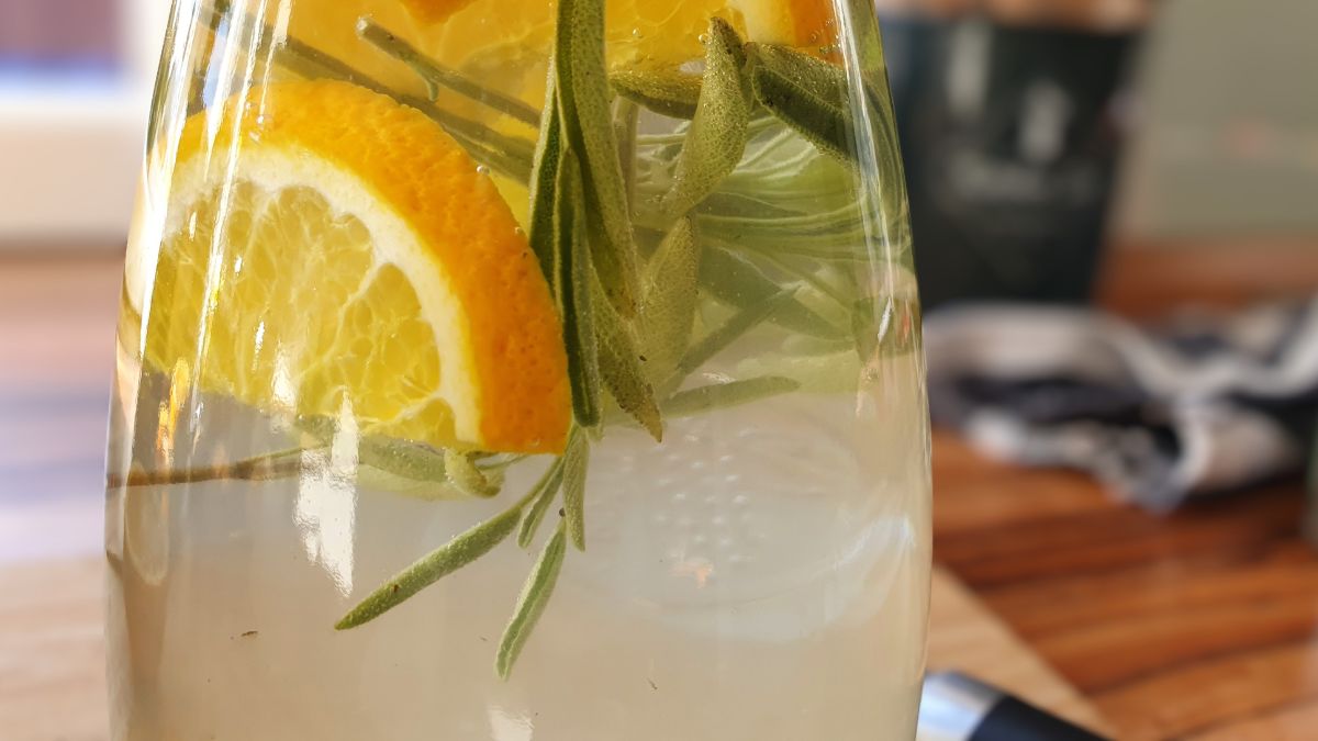 Glaskaraffe gefüllt mit Leitungswasser, Orangenscheiben und Rosmarin-Zweig - selbst gemachtes Infused Water